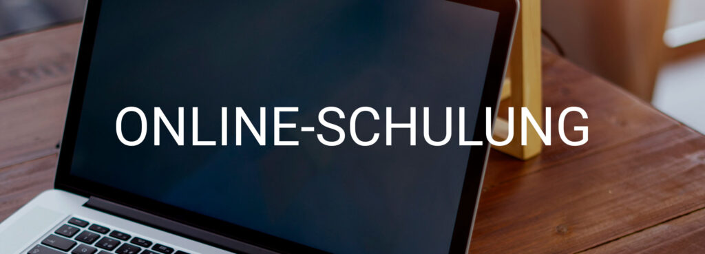 Laptop on a wooden desk with the screen showing the white text ONLINE-SCHULUNG across a dark display.